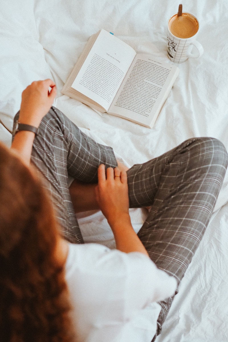 Persona con camisa blanca y pantalón gris acostada en la cama.