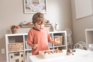 Junge in orangefarbenem T-Shirt mit Rundhalsausschnitt steht vor weißem Holztisch mit Cupcakes