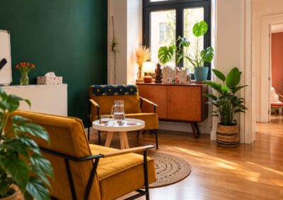Warme Therapielounge mit senfgelben Sesseln, grüner Wand und Pflanzen bei My International Therapy, Berlin
